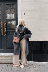 a lady in a black knit top, a beige wide leg knit pants and a grey long wool coat